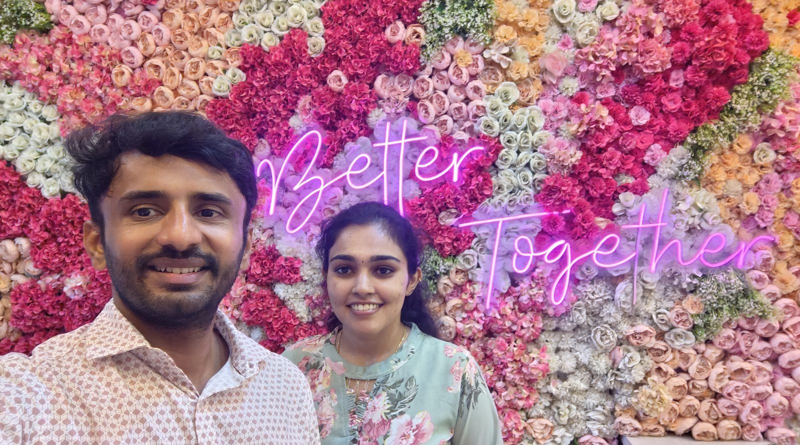 Pawan and Manisha in front of a flower wall with a neon sign reading Better Together